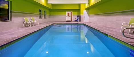 Una piscina interior con agua cristalina azul, rodeada de paredes verdes y suelo de baldosas.