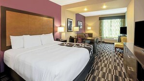 Una habitación de hotel con una cama grande, un escritorio con silla, un televisor y una ventana con cortinas.