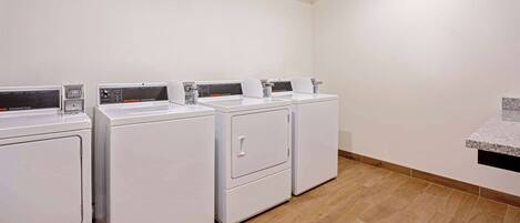 A laundry area with four white washing machines and a granite countertop.