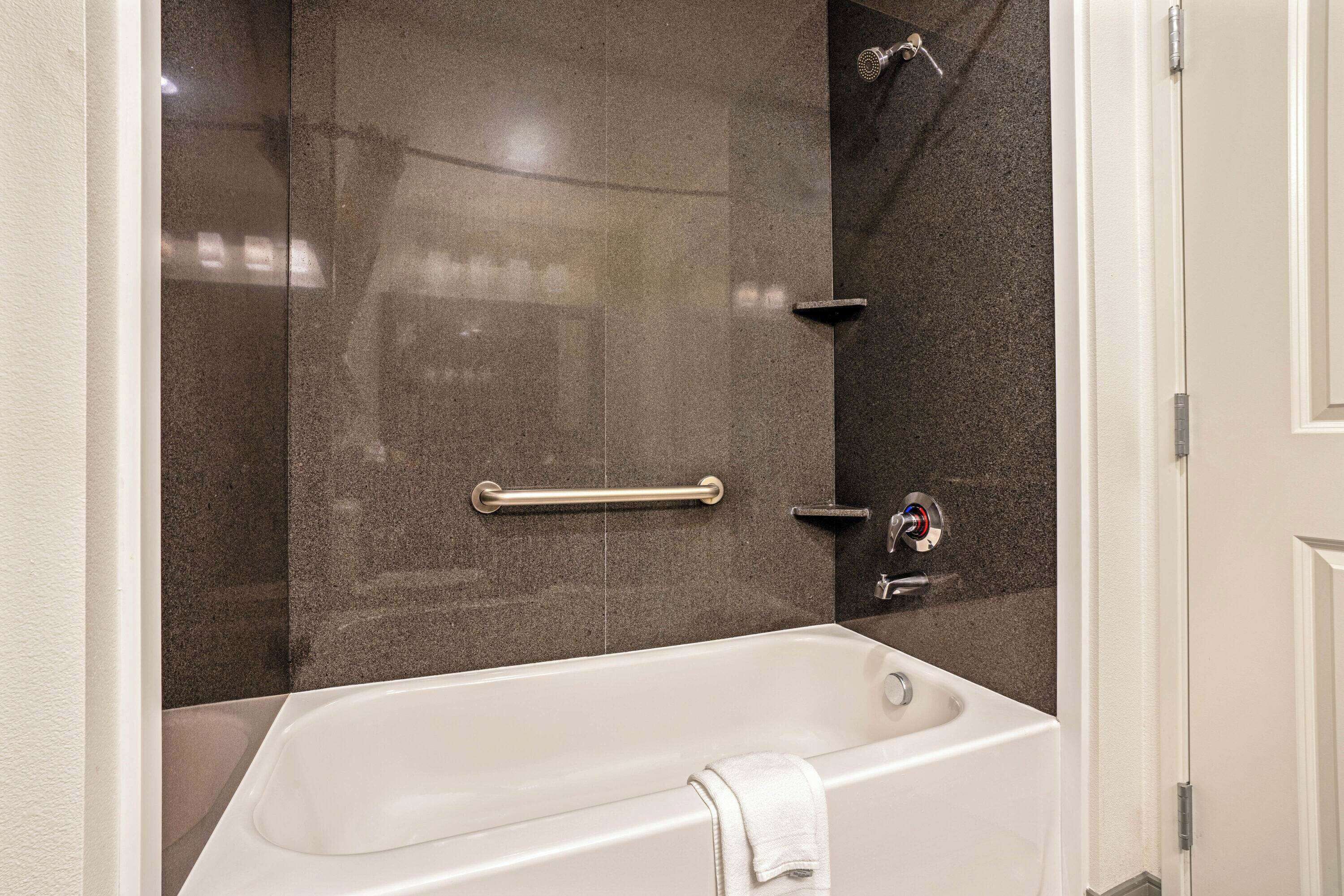 A modern bathroom with a bathtub, a shower area, and a handrail.