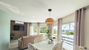 A modern living room with a dining table, white chairs, a beige sofa, and a TV mounted on the wall. - Bubali Villa & Apartments (Oranjestad)