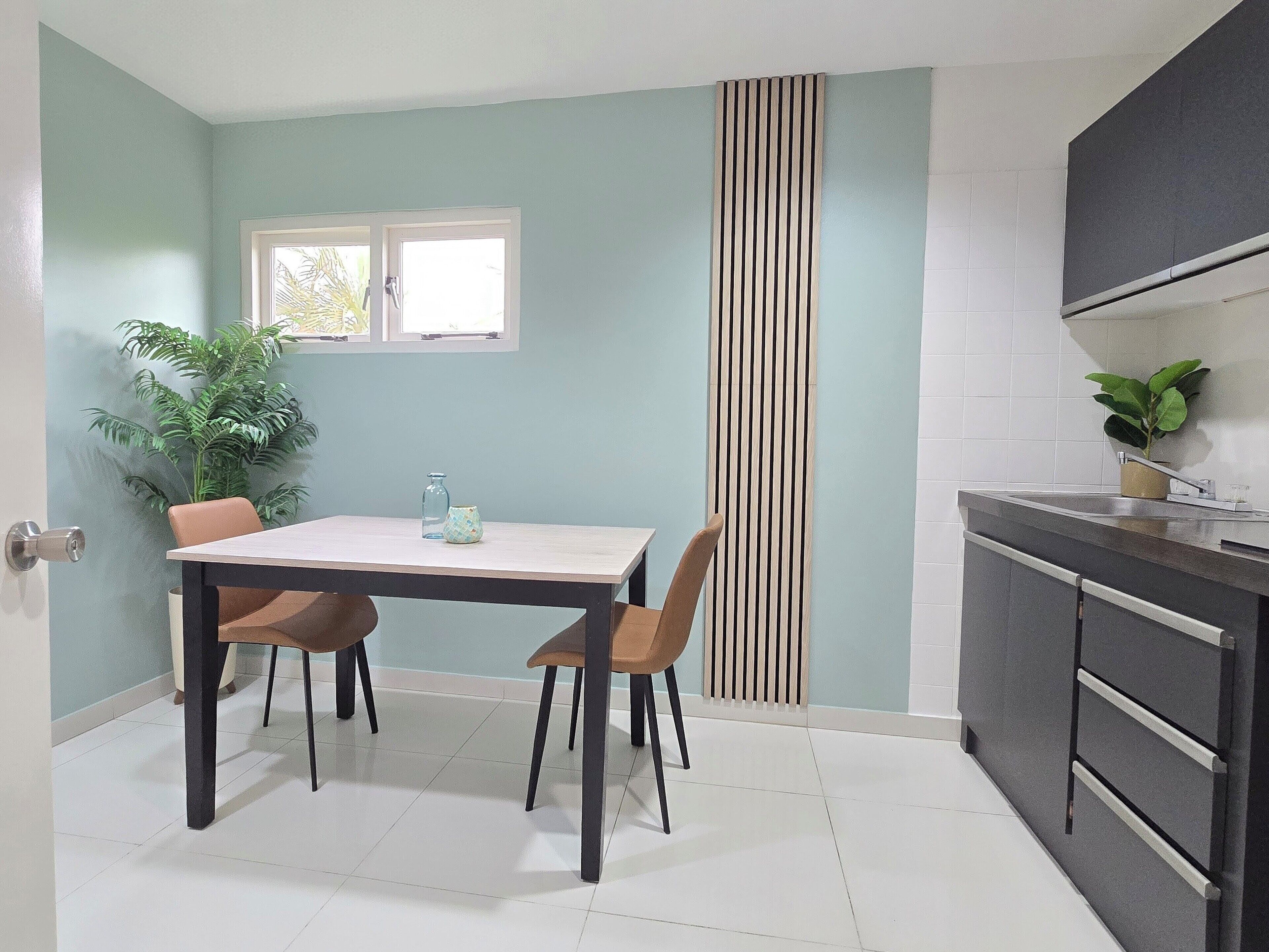 A kitchen with a dining table and chairs, a window, a striped vertical panel, and a potted plant.