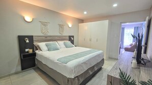 A modern bedroom with a large bed, bedside tables, a wardrobe, and a bathroom visible through an open door. - Bubali Villa & Apartments (Oranjestad)