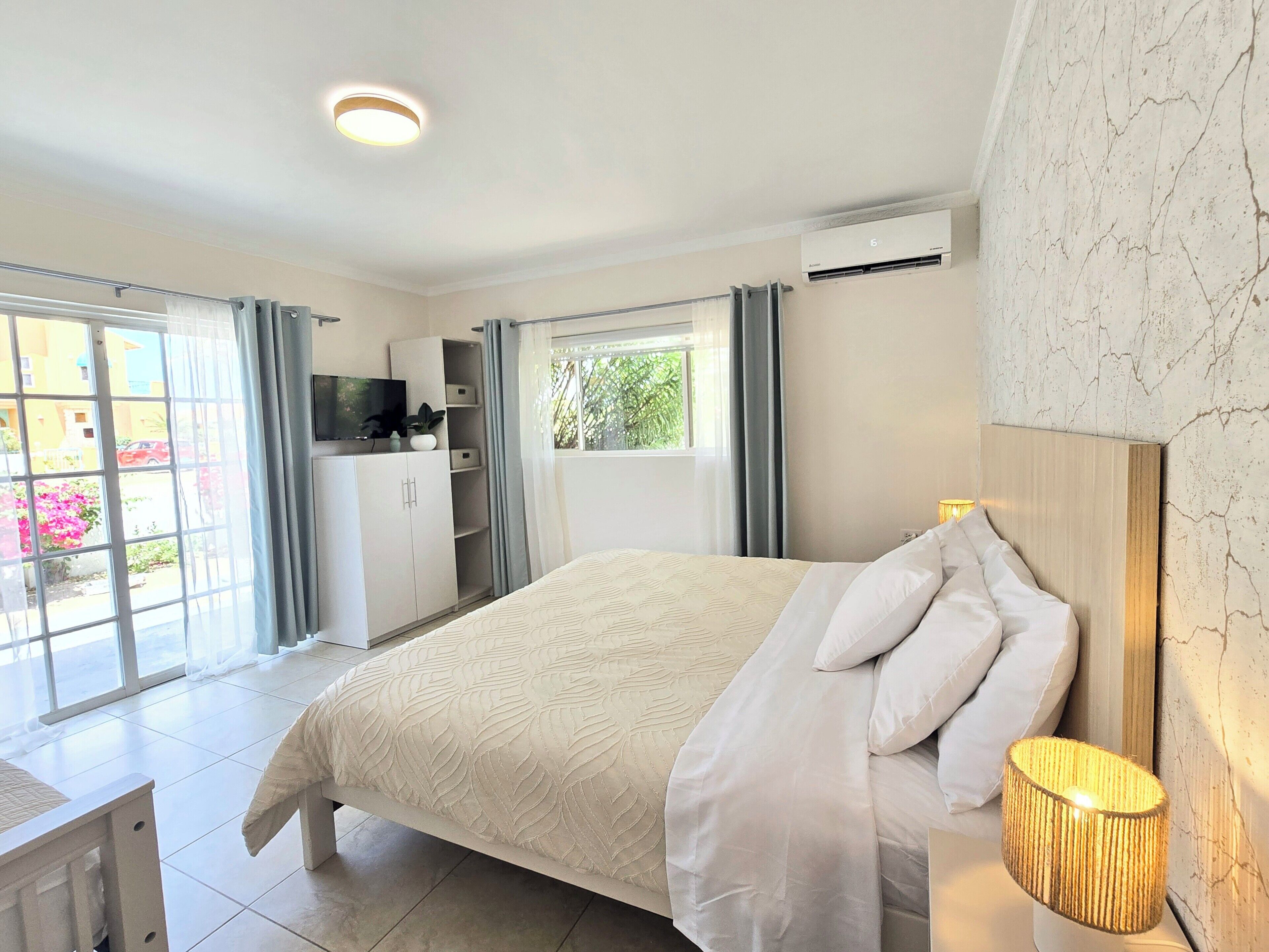 A bedroom with a bed, a bedside lamp, a TV, a wardrobe, and a window with curtains.