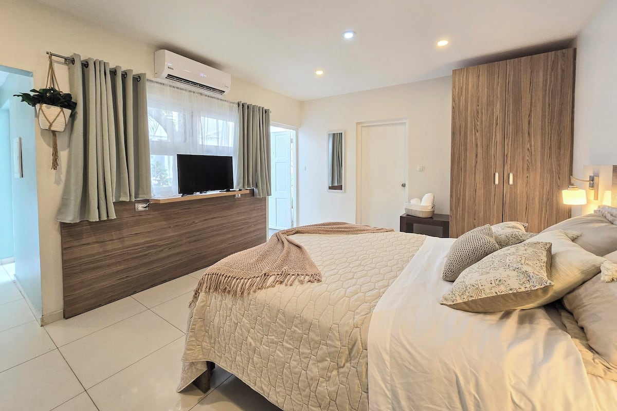 Un dormitorio moderno con una cama grande, un televisor montado en un panel de madera, un armario y una mesita de noche con una lámpara.