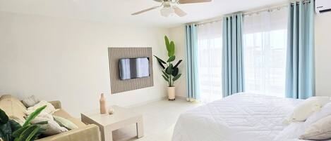 Une chambre d’hôtel moderne avec un grand lit, un téléviseur à écran plat fixé sur un panneau en bois, un ventilateur de plafond et une plante en pot.