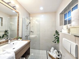 Un baño moderno con ducha de vidrio, tocador de madera, espejo grande y ventana con vistas.