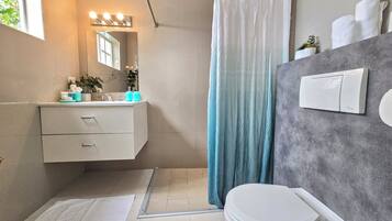 Un baño moderno con un tocador blanco, una cortina de ducha, un inodoro y un perchero para toallas.