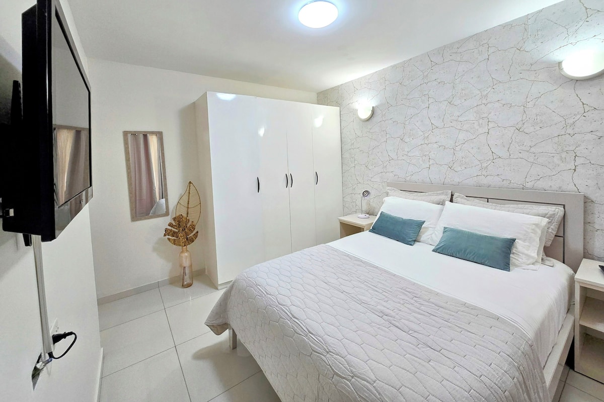 Un dormitorio con cama, armario, televisor y mesita de noche con lámpara.