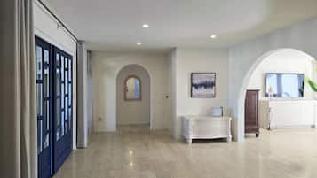 A spacious hallway with a marble floor, a white console table, a framed artwork, and a television on a cabinet.