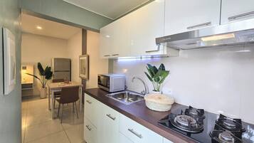 A modern kitchen with white cabinets, a stainless steel sink, a microwave, and a gas stove. There is a dining area with a table and chairs visible in the background.