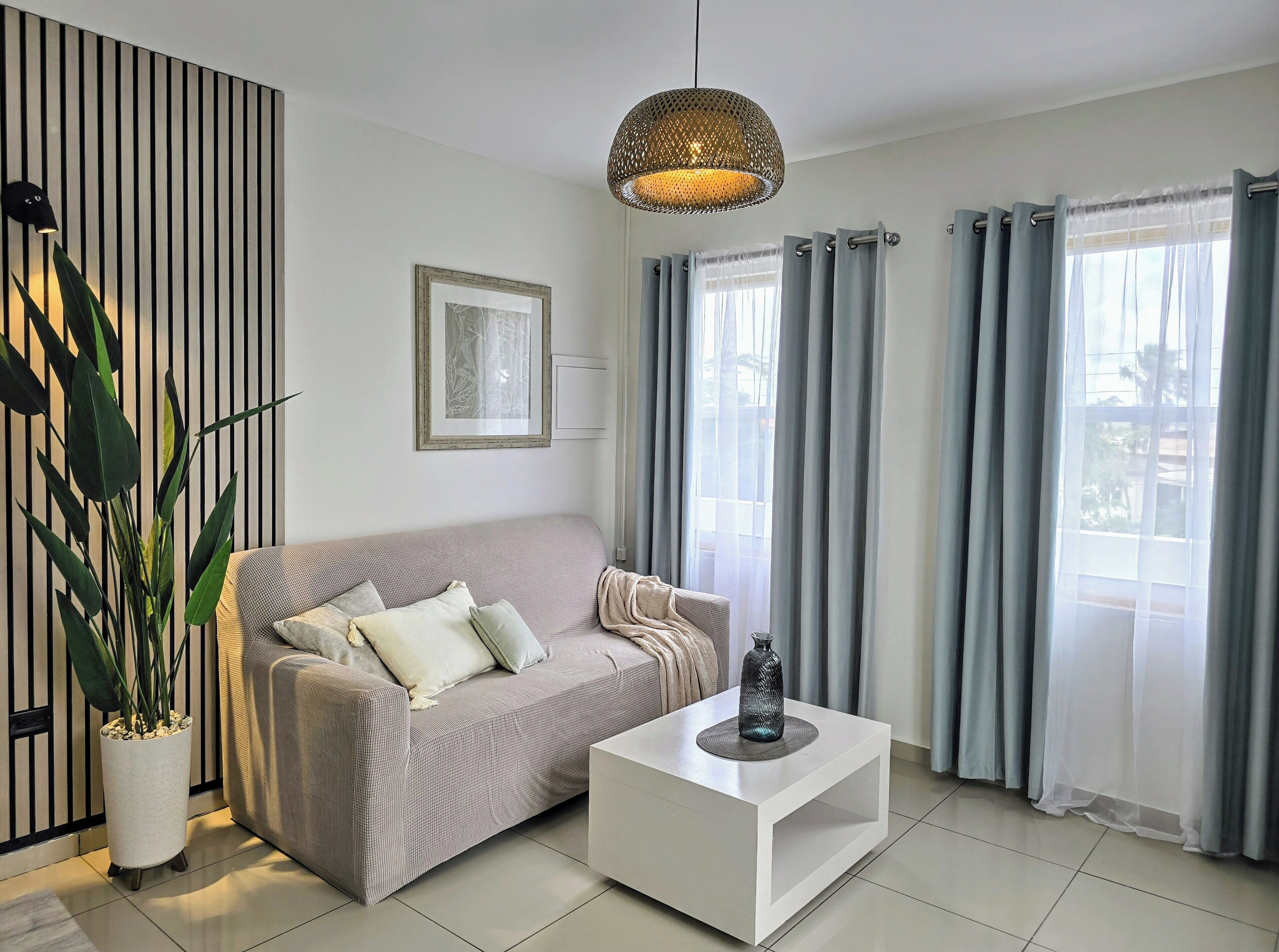 A modern living room with a sofa, a coffee table, a potted plant, a wall-mounted picture, and a ceiling light.