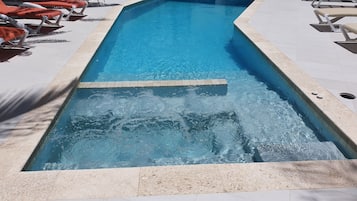 Ein Schwimmbecken mit klarem, blauen Wasser, umgeben von Liegestühlen und einer gefliesten Terrasse.