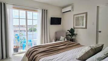 Ein Schlafzimmer mit einem Bett, einem Sessel, einer Topfpflanze und einem Fernseher an der Wand.
