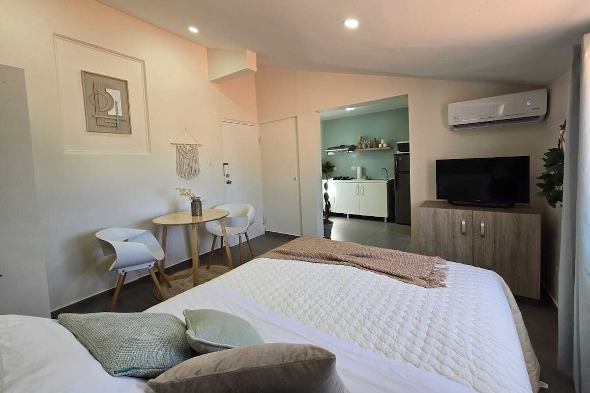 Habitación de hotel con cama, escritorio, silla, kitchenette y televisor.