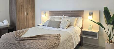 Quarto moderno com cama grande, guarda-roupa de madeira, abajures e um vaso de planta.