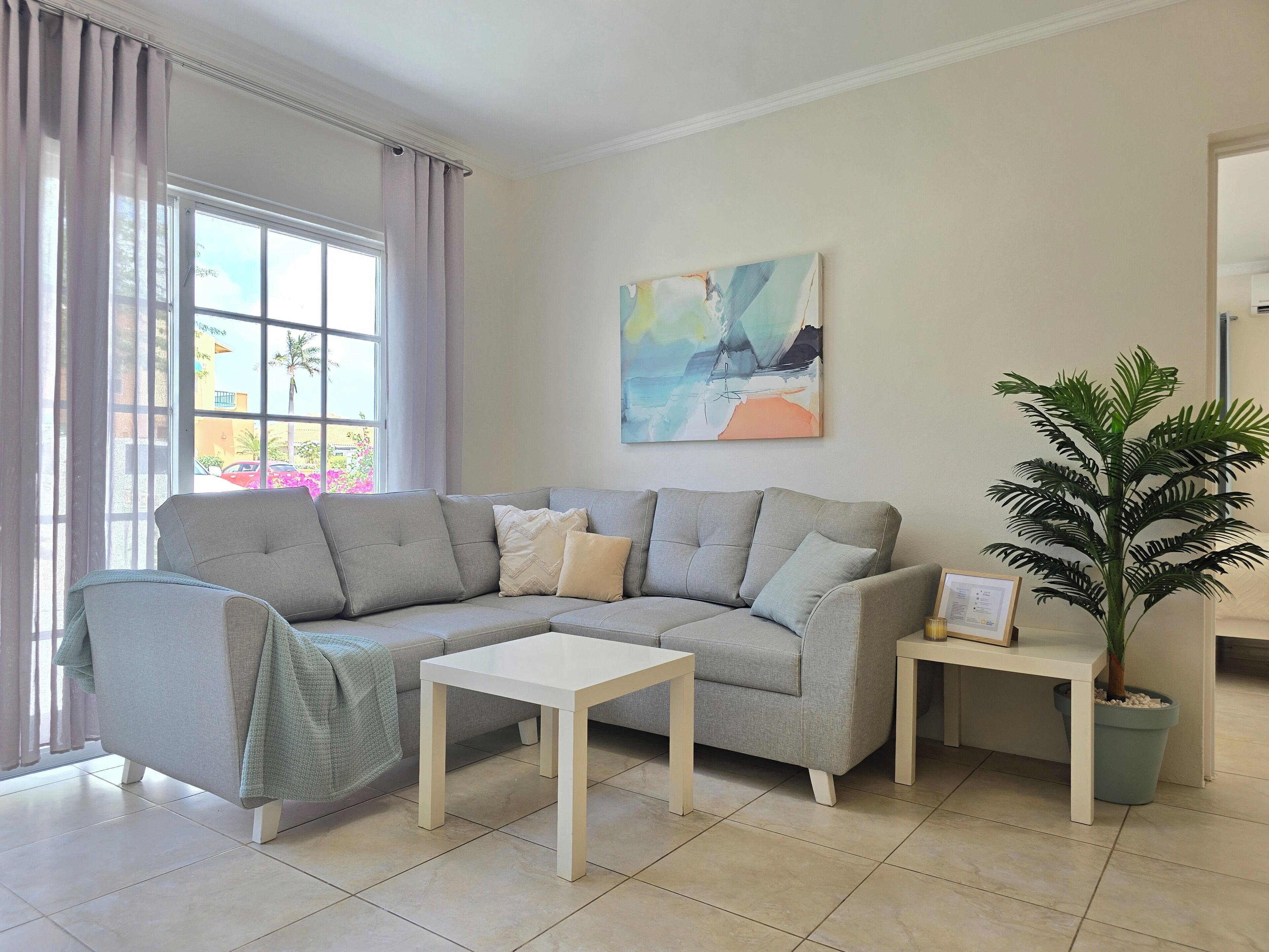 A living room with a grey sofa, a white coffee table, a small side table, and a potted plant.