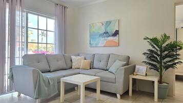 A living room with a grey sofa, a white coffee table, a small side table, and a potted plant.