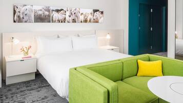 A hotel room with a bed, green sofa, bedside tables, a wall-mounted picture, and a door.