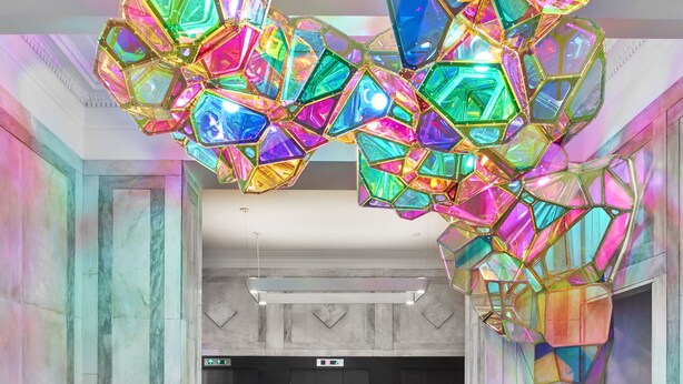 Een ruime lobby met een moderne kroonluchter, marmeren wanden en een lift.