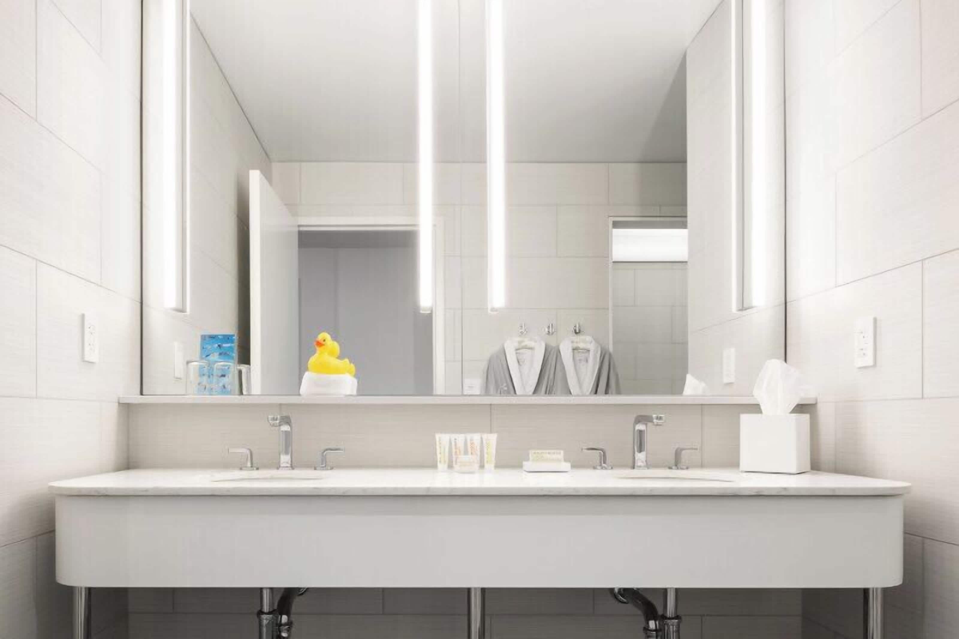 Un baño moderno con un espejo grande, dos lavamanos y un perchero para toallas.