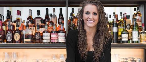 A person seated at a bar with a variety of liquor bottles in the background.