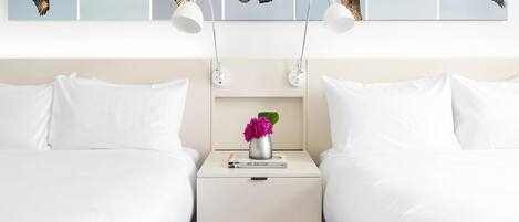 A hotel room with two beds, a nightstand with a vase of flowers, and a wall with five bird paintings.