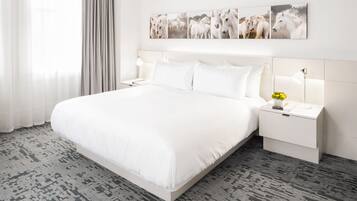 Habitación de hotel con una cama grande, mesitas de noche blancas, una mesita de noche con lámpara y una obra de arte de caballos en la pared.