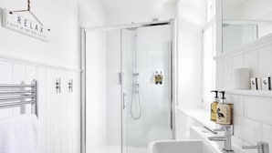 A modern bathroom with a glass-enclosed shower, a white sink with a large mirror, and a towel rack. - Steam Packet Inn (Totnes)