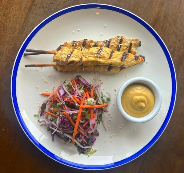 A plate with grilled chicken skewers, a mixed vegetable salad, and a small bowl of sauce.