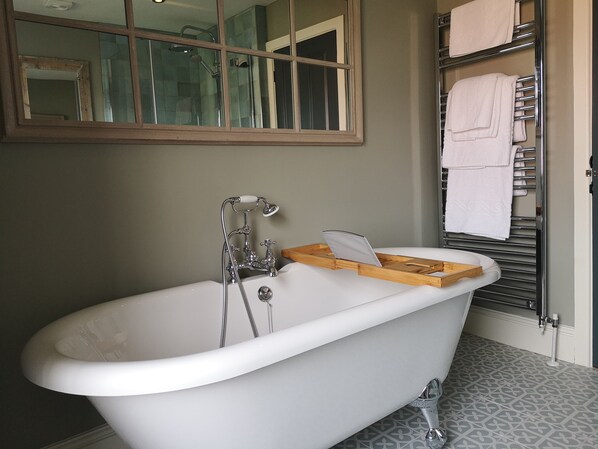A bathroom with a freestanding bathtub, a wooden tray, and a towel rack with folded towels.