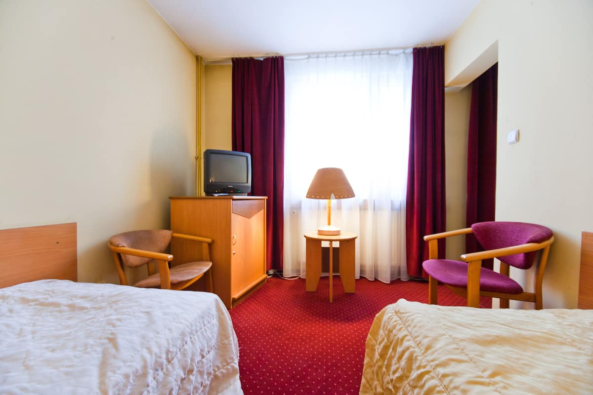 Habitación de hotel con dos camas, televisión, escritorio con lámpara y dos sillones.