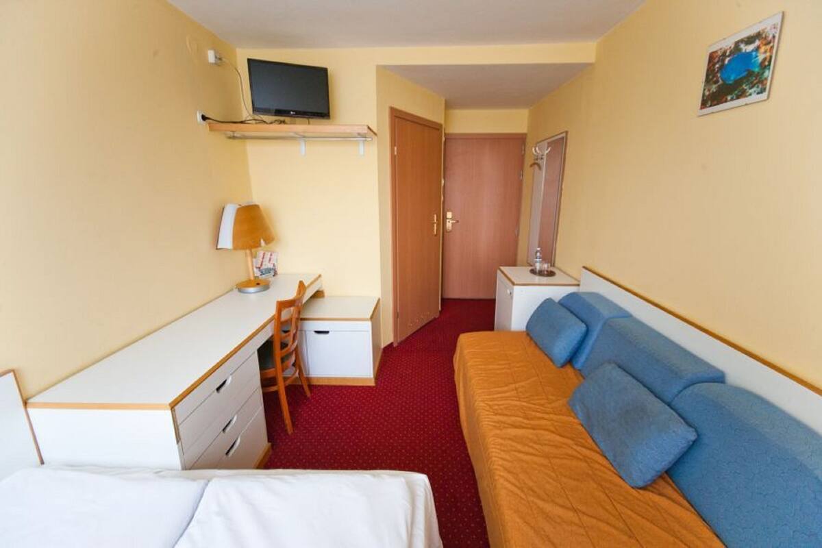 Una habitación de hotel con cama, escritorio, silla, televisor y puerta.
