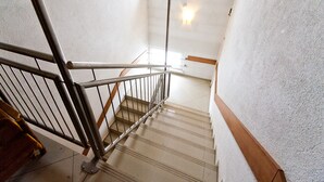 Een trap met metalen leuning en houten handlijsten, die uitkomt op een plateau met een lamp.