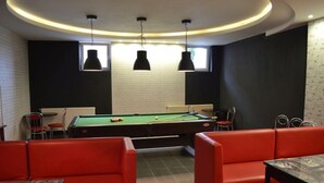 Een biljartkamer met een pooltafel, rode zitplaatsen en hanglampen.