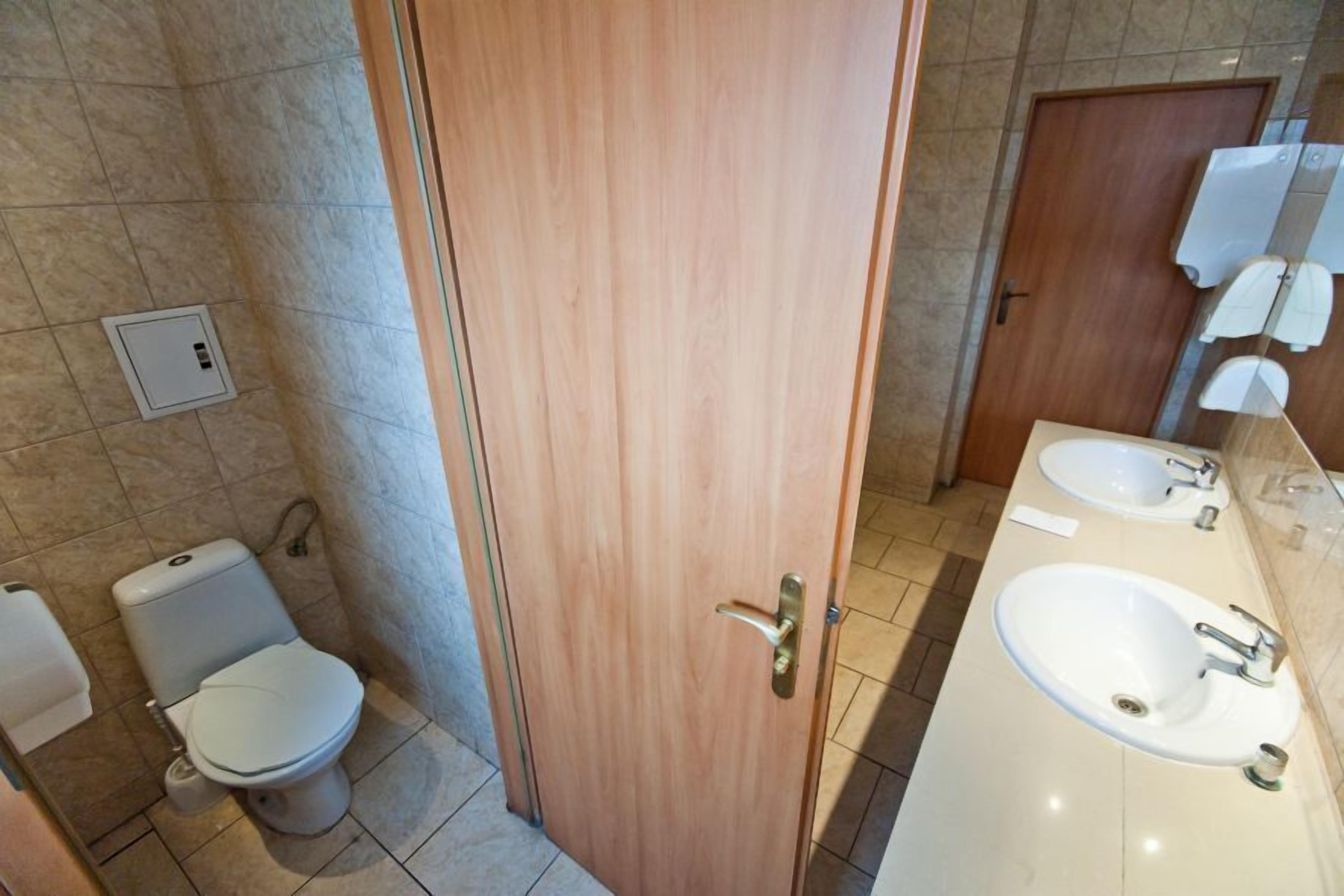 Un baño con puerta de madera, un inodoro y dos lavamanos con espejos.