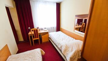 A hotel room with two single beds, a desk with a chair, a window with curtains, and a mirror on the wall.