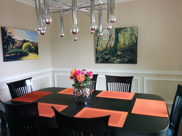 Un coin repas avec une table ronde, des chaises noires, des sets de table orange, un vase avec des fleurs et deux tableaux accrochés aux murs.