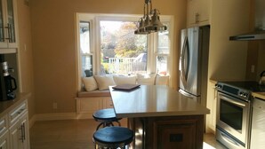A kitchen with a central island, a built-in oven, a refrigerator, and a window seat with cushions.