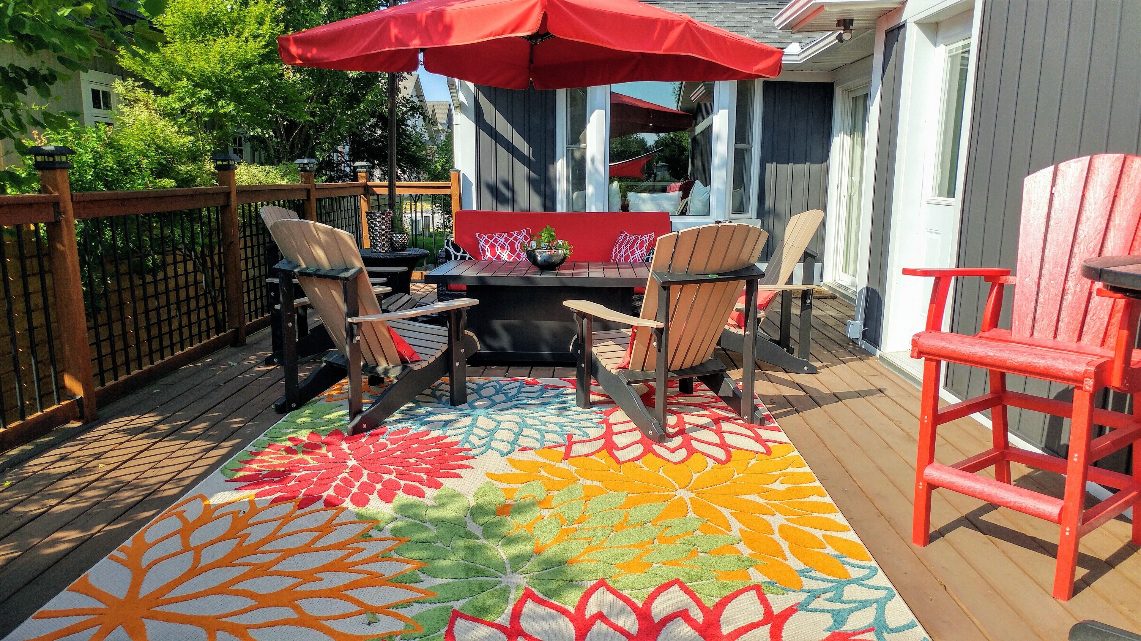 Una terraza con un colorido tapete exterior, sillas rojas y una mesa con sombrilla roja.
