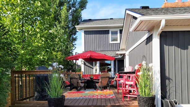A wooden deck with outdoor furniture, a red umbrella, and potted plants.