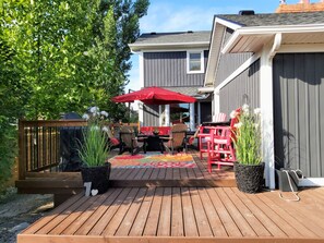 Une terrasse en bois avec des meubles d’extérieur, un parasol rouge et des plantes en pot.