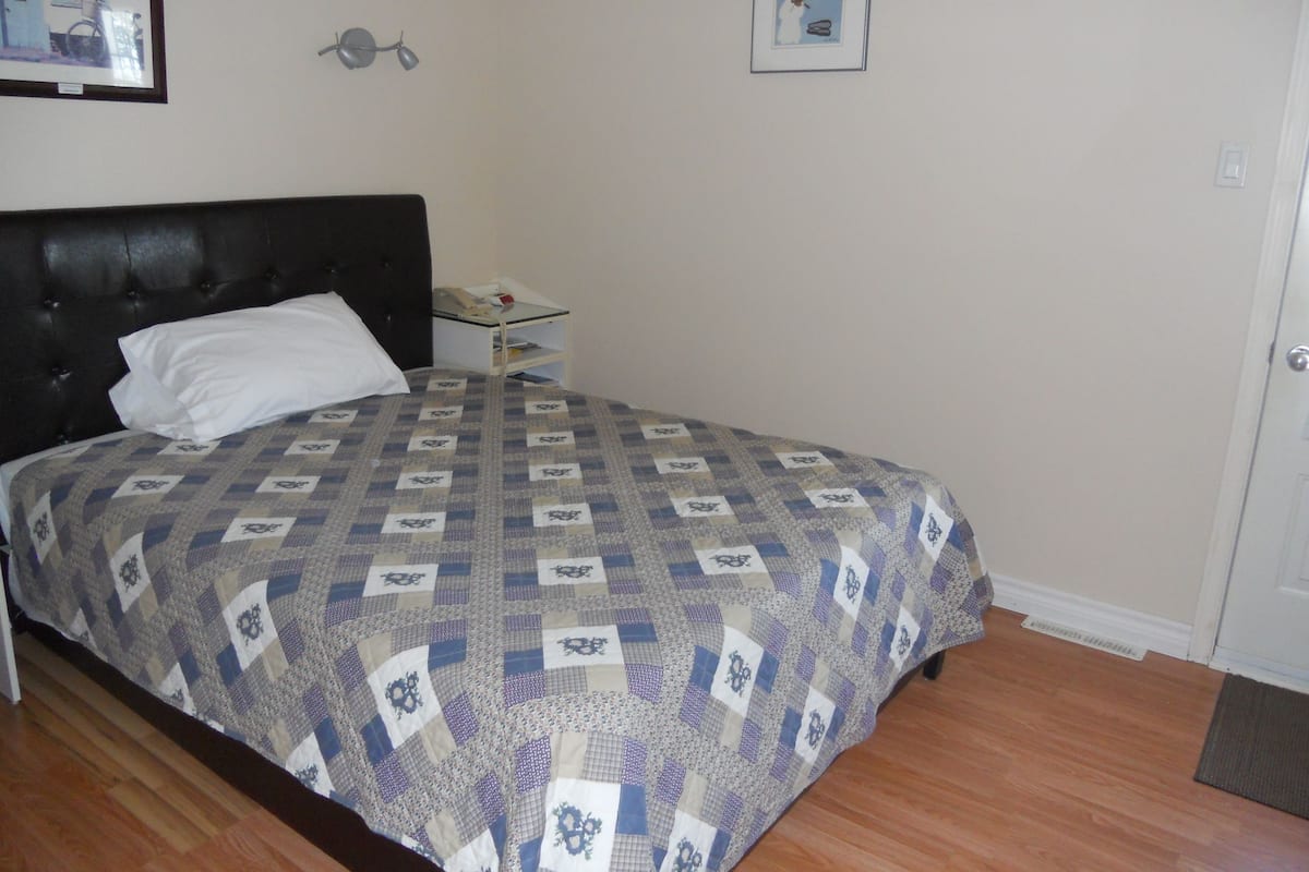 Un dormitorio con cama, mesita de noche, lámpara y puerta.