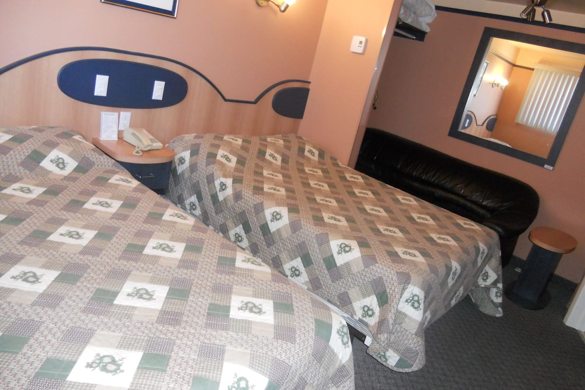 Habitación de hotel con dos camas, una mesita de noche con teléfono, un espejo y una lámpara en la pared.