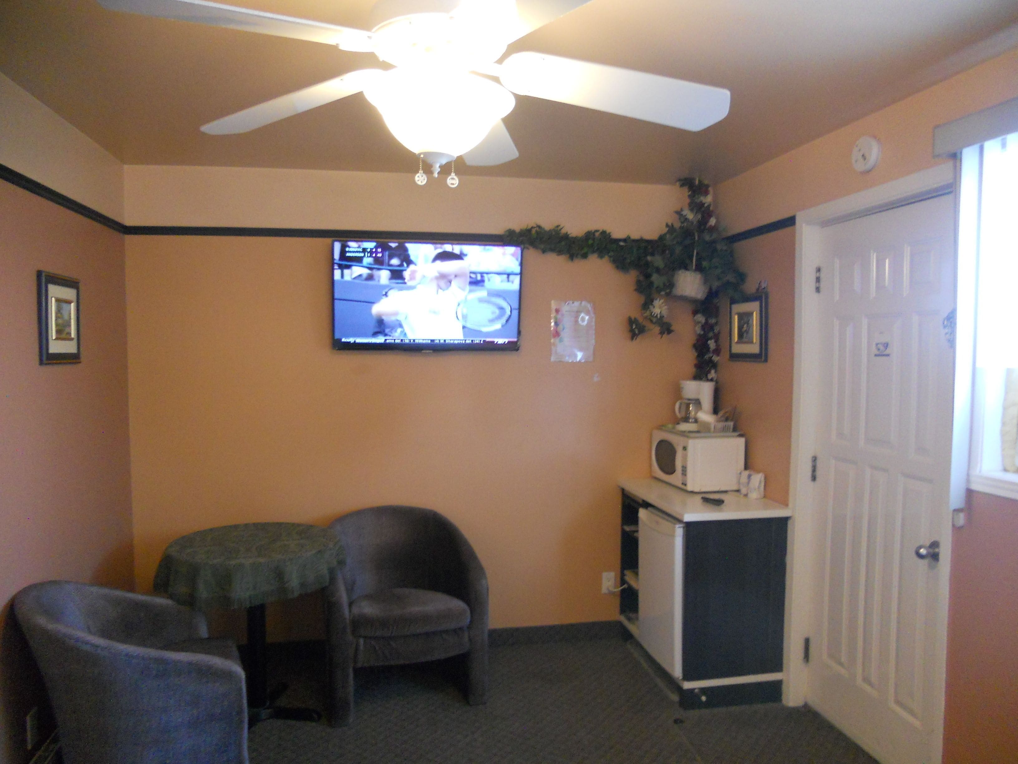 A room with a ceiling fan, a television mounted on the wall, a microwave, and a door.