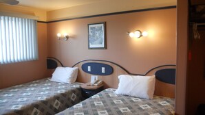 Ett hotellrum med två sängar, en takfläkt, en inramad tavla på väggen och väggmonterade lampor.