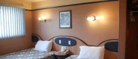 A hotel room with two beds, a ceiling fan, a framed picture on the wall, and wall-mounted lights.