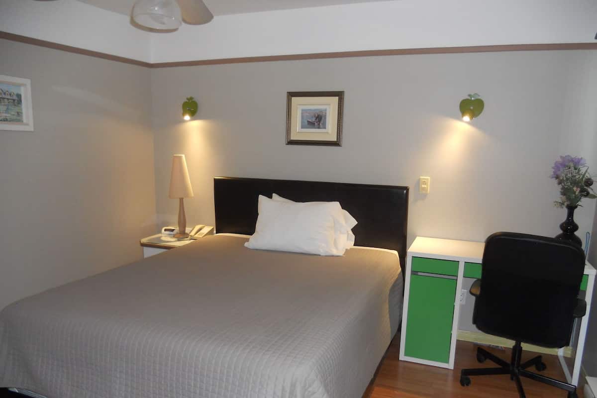 Una cama bien hecha con un edredón blanco, una lámpara de noche, un teléfono y un cuadro en la pared.