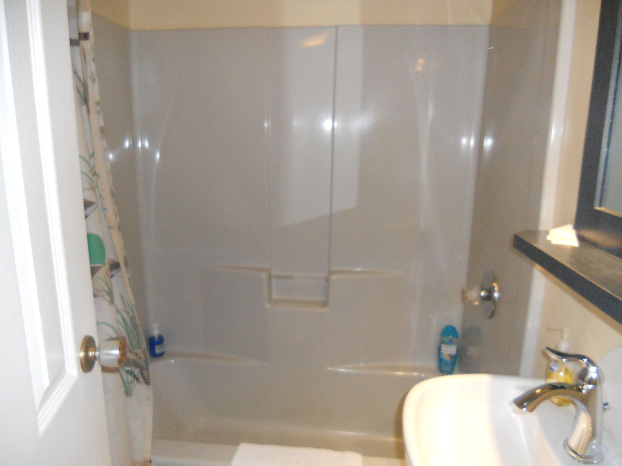 Un baño con ducha envuelta en vidrio, un lavabo blanco y un espejo sobre el lavabo.