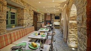 Un comedor de paredes de piedra con mesas y bancos, una chimenea y un televisor.
